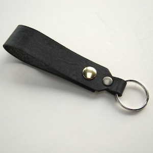 May include: A black leather key chain with a silver key ring and a gold button.