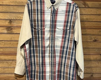 May include: A long-sleeved plaid shirt with a beige collar and sleeves. The plaid pattern features vertical and horizontal stripes in red, navy, brown, and white. The shirt has two chest pockets and a button-down front.