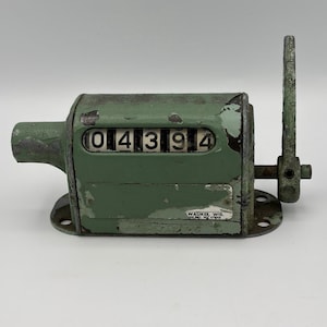 Puede incluir: Contador mecánico verde vintage que muestra el número "04394". Cuenta con un asa lateral y está montado sobre una base de metal. La pintura está desconchada, lo que le da un aspecto rústico. El texto "WAUKEE, WIS." es visible.