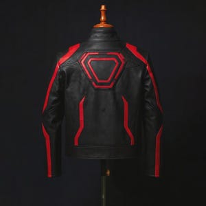 Puede incluir: Chaqueta de cuero negra con detalles rojos. La chaqueta presenta rayas rojas en las mangas y un diseño geométrico en la espalda. Se muestra en una percha de madera sobre un fondo oscuro.
