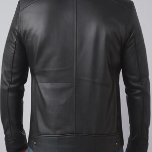 May include: A black leather jacket with a stand-up collar and a tailored fit. The jacket features a vertical seam down the back and two small gold-colored buttons at the waist. The sleeves are long and fitted.