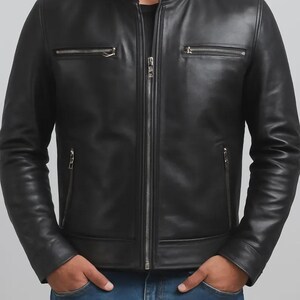 May include: Black leather jacket with a stand-up collar and silver zippers. The jacket has two zippered chest pockets and two side pockets. The model is wearing blue jeans. The jacket is a classic style.