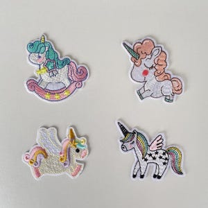 Könnte beinhalten: Vier gestickte Einhorn-Patches in verschiedenen Designs. Eines ist auf einem Schaukelpferd, ein anderes springt, und zwei haben Flügel. Jeder Patch hat Pastellfarben und detaillierte Nähte, ideal für Bastelarbeiten.