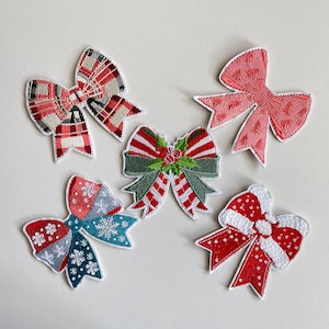 Könnte beinhalten: Eine Sammlung von gestickten Weihnachts-Schleifen-Applikationen in verschiedenen Designs. Die Schleifen haben rote, grüne, weiße und blaue Farben mit Mustern wie Karos, Schneeflocken und Streifen. Jede Schleife hat einen weißen Rand.