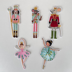 Könnte beinhalten: Gestickte Aufnäher mit Figuren aus dem Ballett Der Nussknacker. Das Set enthält einen Nussknacker-Soldaten, einen Mäusekönig, eine Mäusekönigin, eine Fee und eine Ballerina. Jeder Aufnäher ist farbenfroh mit detaillierten Nähten.