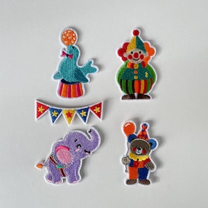 Könnte beinhalten: Set aus fünf farbenfrohen, gestickten Aufnähern zum Thema Zirkus. Enthält einen türkisfarbenen Seehund, der einen Ball balanciert, einen Clown, ein Banner, einen lila Elefanten und einen Bären mit einem Ballon. Ideal zum Dekorieren von Kleidung oder Accessoires.