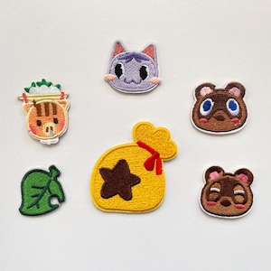 Könnte beinhalten: Gestickte Aufnäher mit Motiven aus Animal Crossing. Das Set enthält Gesichter von Charakteren, ein Blatt und einen Geldsack, alle in leuchtenden Farben. Ideal zum Verzieren von Kleidung oder Taschen.