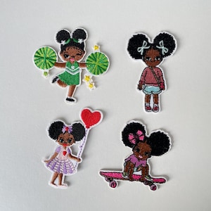 Pode incluir: Conjunto de quatro patches bordados com meninas de desenho animado com pele escura e grandes afro. Uma é uma líder de torcida, outra segura um balão de coração, uma anda de skate e a última usa uma camisa e shorts rosa.