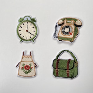 Op de afbeelding: Een set van vier geborduurde patches met een groene wekker, een groene draaischijftelefoon, een crèmekleurig schort met een rood bloemmotief en een groene tas met bruine riemen. Elke patch is voorzien van een witte rand en gedetailleerd stikwerk.