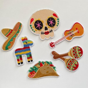 Könnte beinhalten: Gestickte Aufnäher mit einem Sombrero, einem Zuckerschädel, einer Gitarre, Maracas, einer Piñata und einem Taco. Die Aufnäher sind in verschiedenen Farben gehalten, darunter Gelb, Rot, Grün, Blau und Braun, und haben einen weißen Rand.