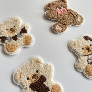 Pode incluir: Quatro patches bordados de ursinhos em v&aacute;rias cores. Dois s&atilde;o creme com detalhes castanhos, um &eacute; castanho com um la&ccedil;o rosa e outro &eacute; creme com um cachecol. Ideais para projetos de costura ou artesanato.