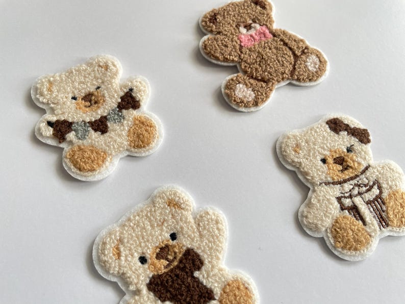 Pode incluir: Quatro patches bordados de ursinhos em v&aacute;rias cores. Dois s&atilde;o creme com detalhes castanhos, um &eacute; castanho com um la&ccedil;o rosa e outro &eacute; creme com um cachecol. Ideais para projetos de costura ou artesanato.