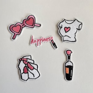 Puede incluir: Parches bordados con gafas de sol rosas en forma de corazón, una camiseta blanca con un corazón rosa, una botella de vino, una mano con uñas rosas y la palabra "happiness" con un lápiz labial.