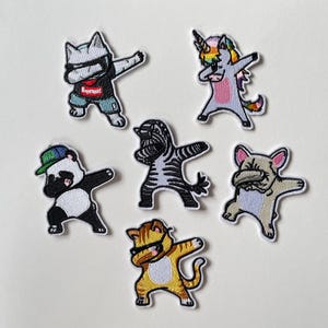 Op de afbeelding: Een set van zes geborduurde patches met verschillende dieren, waaronder een kat, eenhoorn, panda, zebra, hond en tijger, allemaal afgebeeld in een dabbing pose. Elke patch heeft eigen kleuren en patronen, zoals de kat met een rood-zwart shirt.