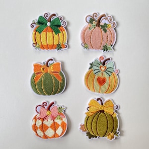 Puede incluir: Seis parches bordados de calabaza dispuestos en dos columnas. Cada calabaza presenta un diseño único con varios colores como naranja, verde, amarillo y rosa, acentuados con lazos decorativos, hojas y formas de corazón en costuras detalladas.