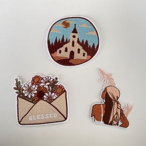 May include: Three embroidered patches: a church scene in a circle, a floral envelope with "Blessed" text, and a woman with a headscarf. The church patch features a beige building, brown trees, and a blue sky.