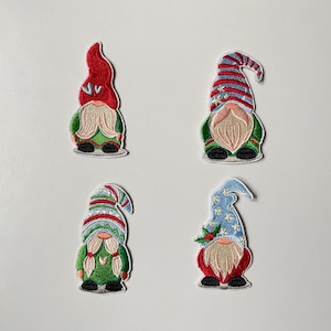 Könnte beinhalten: Vier gestickte Zwergenaufnäher mit verschiedenen Hutdesigns. Jeder Zwerg hat einen weißen Bart, einen grünen Körper und schwarze Schuhe. Die Hüte sind rot, blau und gestreift mit Rot, Weiß und Blau. Ein festlicher, weihnachtlicher Bastelartikel.