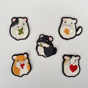 Puede incluir: Cinco parches bordados con hámsters de dibujos animados en varios colores. Cada hámster tiene un contorno negro y sostiene un pequeño objeto, como un trébol de cuatro hojas o un corazón. Los parches están sobre un fondo blanco.