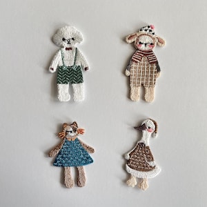 Op de afbeelding: Vier geborduurde stoffen patches met antropomorfe dieren. Een witte hond in een groene tuinbroek, een beige lammetje in een geruite outfit met muts, een bruine kat in een blauwe jurk en een wit-bruine gans met een bruine trui en muts.