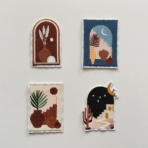 Könnte beinhalten: Vier gestickte Aufnäher mit Wüsten- und botanischen Themen. Jeder Aufnäher zeigt ein anderes Design, darunter Vasen, Pflanzen und Torbögen, in Braun-, Blau- und Beigetönen. Die Aufnäher haben einen weißen Rand.