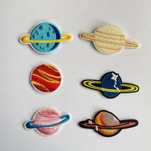 Puede incluir: Parches bordados con diseños de planetas coloridos. Incluye planetas con tonos azules, amarillos, rojos y rosas, con detalles como anillos y superficies texturizadas. Ideales para decorar ropa o accesorios.