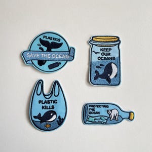 May include: Four blue embroidered patches with ocean-themed designs. One patch says "Plastics Save the Ocean" with a whale tail. Another says "Keep Our Oceans" with a whale in a jar. A third says "Plastic Kills" with a whale. The last says "Protecting the Ocean" with a polar bear.
