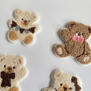 Pode incluir: Quatro patches bordados de ursinhos em v&aacute;rios tons de castanho e creme. Cada urso tem um design &uacute;nico, incluindo um cachecol, la&ccedil;o e detalhes decorativos. Os patches est&atilde;o em um fundo branco.