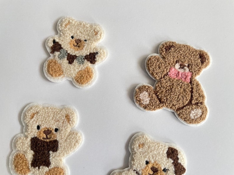 Pode incluir: Quatro patches bordados de ursinhos em v&aacute;rios tons de castanho e creme. Cada urso tem um design &uacute;nico, incluindo um cachecol, la&ccedil;o e detalhes decorativos. Os patches est&atilde;o em um fundo branco.
