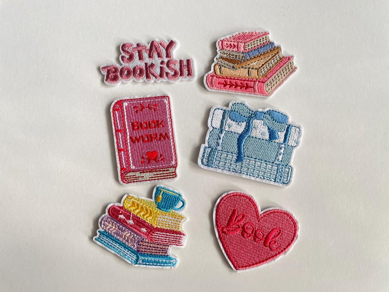 May include: Embroidered patches with book-related designs. The set includes patches depicting stacks of books, a heart with the word "Book", and the phrases "Stay Bookish" and "Book Worm". The patches are in various colours, including pink, blue, and yellow.
