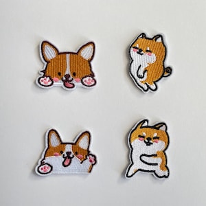 Könnte beinhalten: Vier aufgestickte Aufnäher mit Cartoon-Hunden. Zwei Aufnäher zeigen Corgis in Braun, Weiß und Rosa, während die anderen beiden Shiba Inus in Orange, Weiß und Rosa zeigen. Jeder Aufnäher hat einen weißen Rand.