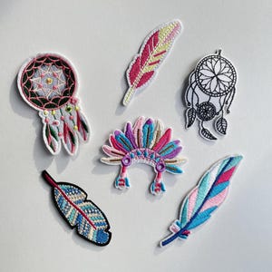 Puede incluir: Un conjunto de parches bordados con diseños de inspiración nativa americana. Los parches incluyen atrapasueños, plumas y un tocado, en una variedad de colores como rosa, azul y turquesa. Los parches están sobre un fondo blanco.