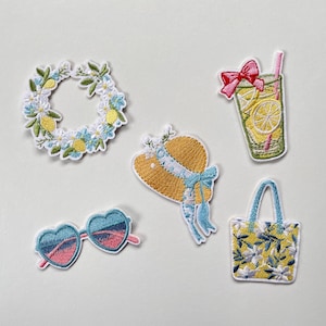 May include: A set of five embroidered patches featuring a circular floral wreath with lemons, a glass of lemonade with a pink bow and straw, a yellow sun hat with a blue ribbon, heart-shaped sunglasses, and a yellow tote bag with a floral pattern.