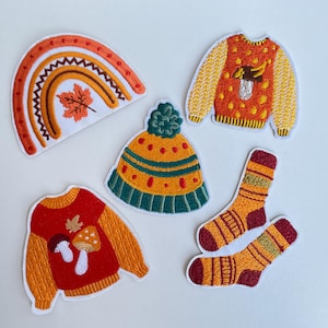 Könnte beinhalten: Eine Sammlung von aufgestickten Aufnähern mit Herbstmotiven. Enthält einen Regenbogen, eine Mütze, zwei Pullover und ein Paar Socken. Die Aufnäher sind in Orange-, Rot-, Gelb- und Grüntönen gehalten und weisen detaillierte Stickereien auf.