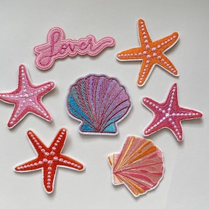 Peut inclure: Écussons brodés avec une inscription « Lover », des étoiles de mer et des coquillages dans les tons de rose, orange et bleu. Les écussons ont des bordures blanches et sont destinés à un usage décoratif.
