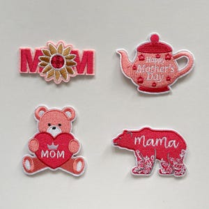 Puede incluir: Cuatro parches bordados con temática del Día de la Madre. Incluye un "MOM" rosa con un girasol, una tetera con "Happy Mother's Day", un oso de peluche con un corazón con "MOM" y un oso con "mama".