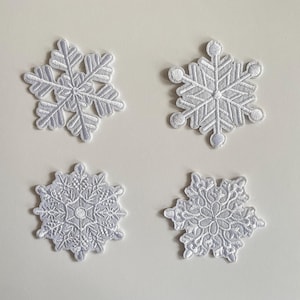 May include: Four white snowflake patches with detailed embroidery. Each patch has a unique design, displaying delicate patterns and shapes. These patches are suitable for winter-themed crafts and clothing.