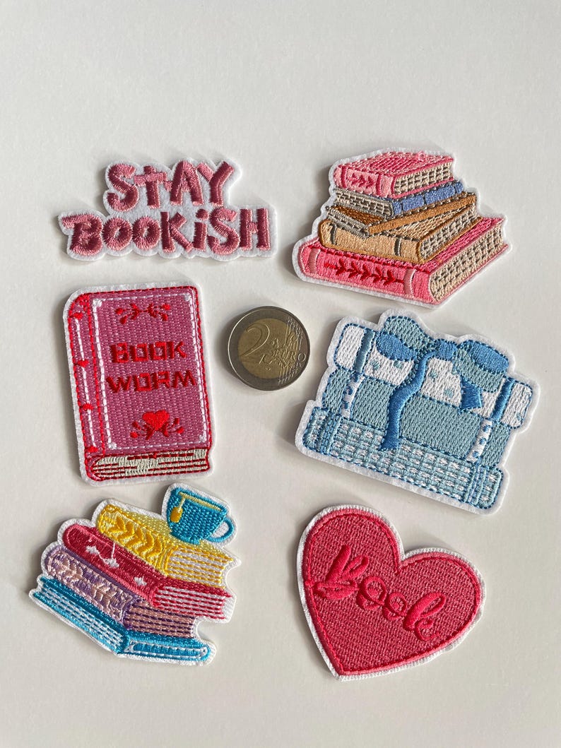 May include: Embroidered patches with a book theme. The patches feature stacks of books in different colours, a heart with the word "Book", and the phrase "Stay Bookish". A coin is also present.