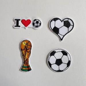 May include: Four embroidered patches with football themes. One patch says "I ♥ football" with a red heart. Other patches include a football in a heart shape, a football, and a gold trophy.