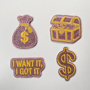 Puede incluir: Cuatro parches bordados con un diseño brillante en morado y amarillo. El conjunto incluye una bolsa de dinero con un signo de dólar, un cofre del tesoro, un símbolo de dólar y un parche rectangular con el texto I WANT IT, I GOT IT.