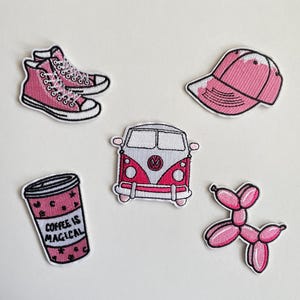 Könnte beinhalten: Eine Sammlung von pinkfarbenen, gestickten Aufnähern. Sie zeigen ein Paar High-Top-Sneaker, eine Baseballkappe, einen Kaffeebecher mit Text, einen VW-Bus und ein Ballon-Tier.