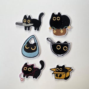 以下が含まれることがあります： 大きな黄色い目をした黒猫の刺繍ワッペン6枚セット。ナイフを持つ猫、バスケットに入った猫、青いバッグに入った猫、ボウルに入った猫、赤い毛糸で遊ぶ猫、段ボール箱に入った猫のデザインがそれぞれ刺繍されています。