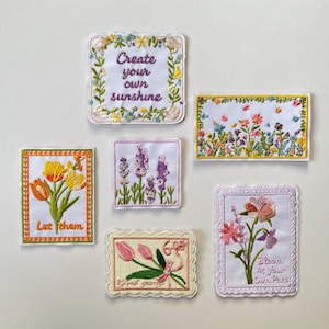 Puede incluir: Seis parches de tela bordados rectangulares y cuadrados con diseños florales y texto. Los parches incluyen frases como Create your own sunshine, Let them y Bloom at your own pace, rodeadas de coloridas flores bordadas y bordes decorativos.