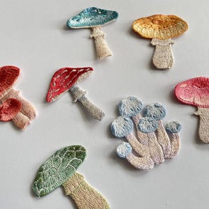May include: Embroidered mushroom patches in various colors, including red, pink, blue, green, and orange. Each patch features detailed stitching and a stem. These patches are ideal for adding a whimsical touch to clothing or accessories.