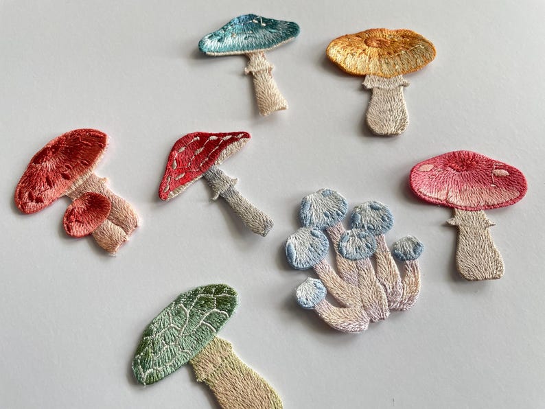 May include: Embroidered mushroom patches in various colors, including red, pink, blue, green, and orange. Each patch features detailed stitching and a stem. These patches are ideal for adding a whimsical touch to clothing or accessories.