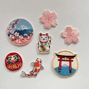 May include: A white ceramic mug with a black handle and the text "But First, Coffee" in a bold, black font. The mug is set against a blurred background, suggesting a cozy setting.