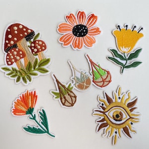 May include: A collection of embroidered patches featuring various designs. Included are a mushroom cluster, orange flower, yellow flower, several plant-themed patches, an orange flower, and a sun with an eye design. Each patch has a white border.