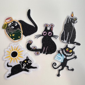 Peut inclure: Ensemble de patchs brodés représentant des chats noirs dans diverses poses. Les motifs incluent un chat dans une bouteille de potion, un chat avec une couronne de fleurs, un chat bougie, un chat courant, un chat avec un soleil et un chat tenant un sac "Take Out".