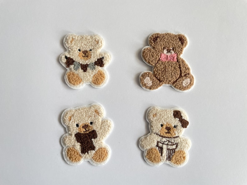 Pode incluir: Quatro patches bordados de ursinhos de pel&uacute;cia em creme e castanho. Cada urso tem um detalhe diferente de cachecol ou la&ccedil;o. Os ursos t&ecirc;m corpos cor de creme, patas castanhas e detalhes castanhos ou creme.