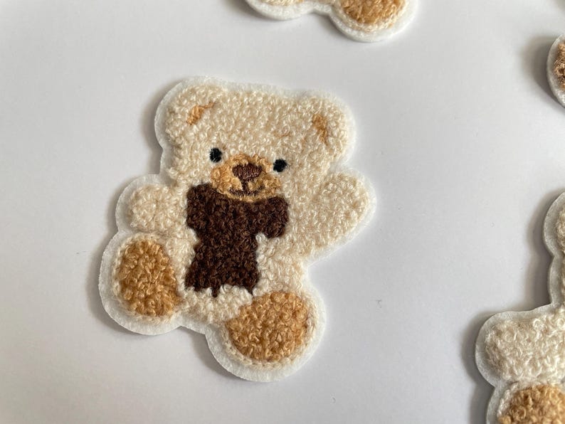 Pode incluir: Patches bordados de ursinho de pel&uacute;cia em creme, castanho e bege. Os patches apresentam um design de ursinho de pel&uacute;cia com um cachecol castanho. Os patches est&atilde;o em um fundo branco. Ideais para roupas ou acess&oacute;rios.