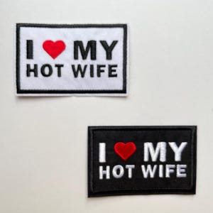 Könnte beinhalten: Zwei rechteckige Aufnäher mit dem Text "I ❤️ MY HOT WIFE". Einer ist weiß mit schwarzem Rand, der andere ist schwarz mit weißem Text und Rand. Das Herzsymbol ist rot.
